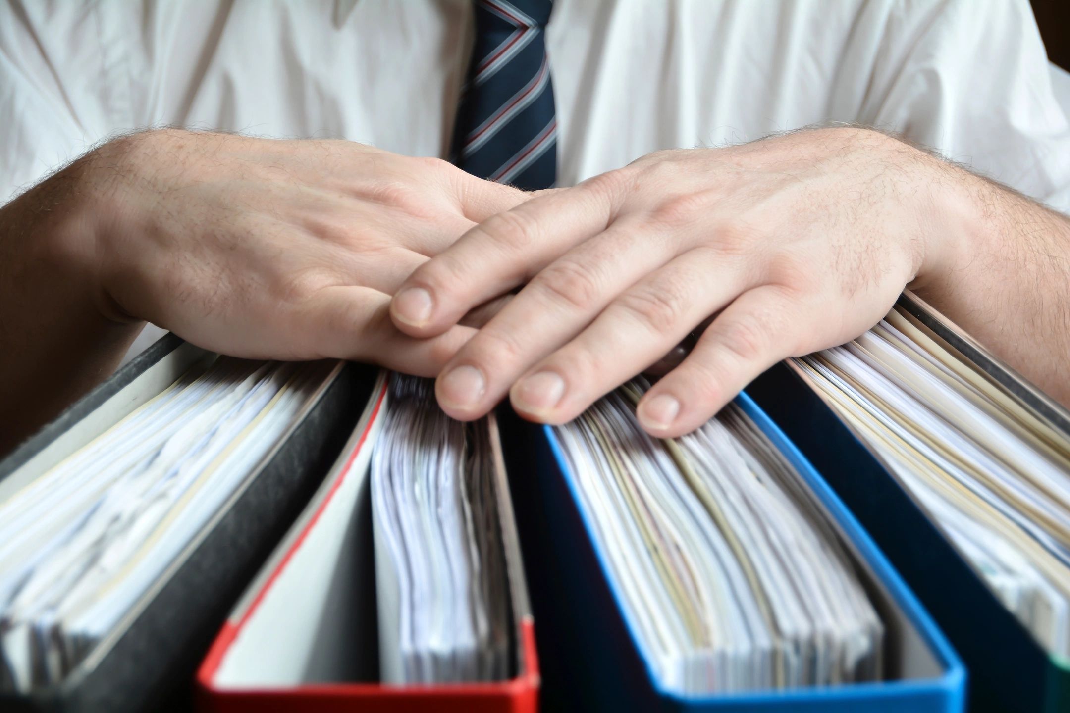 Man's hands on top of four binders with papers